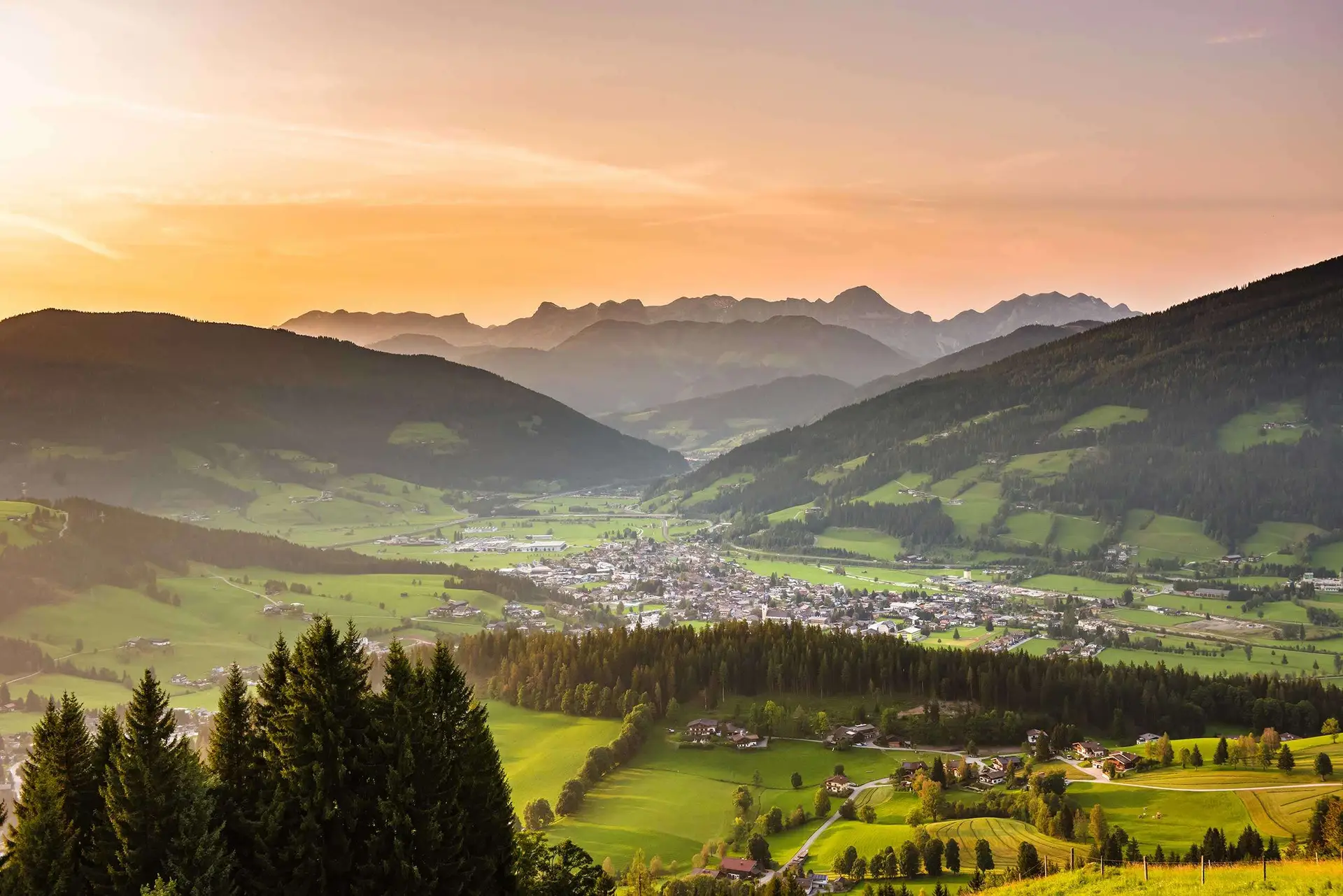 Blick über Altenmarkt und das Tal auf die Bergkette der Salzburger Sportwelt im Abendlicht